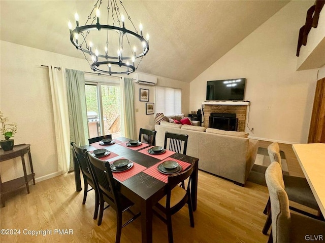 dining area featuring light hardwood / wood-style flooring, lofted ceiling, a stone fireplace, an inviting chandelier, and a wall mounted air conditioner