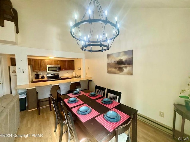 dining space with a baseboard radiator, a towering ceiling, a chandelier, and light hardwood / wood-style floors