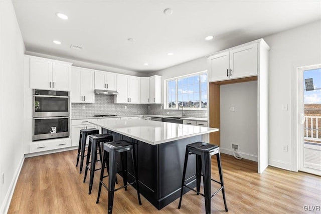 kitchen featuring white cabinets, light hardwood / wood-style floors, a center island, and stainless steel double oven