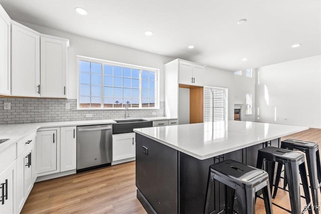 kitchen featuring dishwasher, white cabinets, sink, a kitchen island, and light wood-type flooring