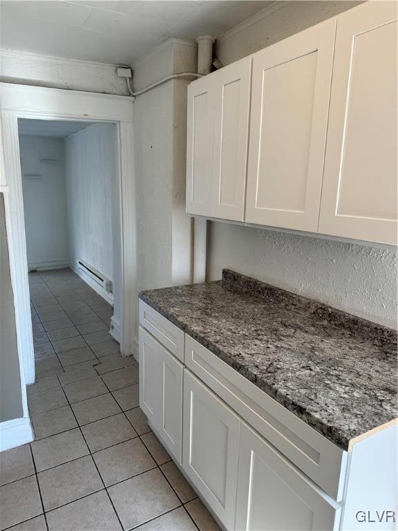 kitchen featuring dark stone countertops, light tile patterned flooring, a baseboard heating unit, and white cabinetry