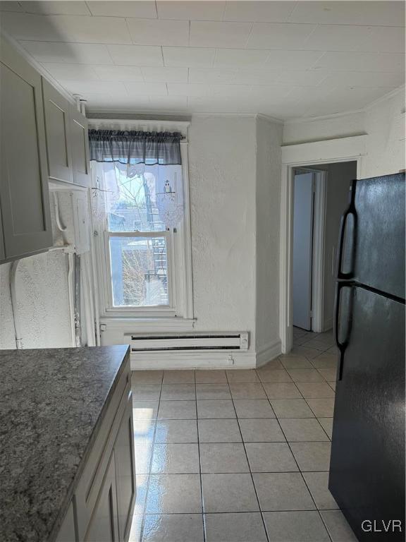 kitchen featuring gray cabinets, a baseboard heating unit, light tile patterned floors, ornamental molding, and black refrigerator