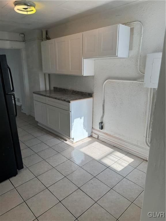 kitchen featuring white cabinetry, black refrigerator, and light tile patterned floors