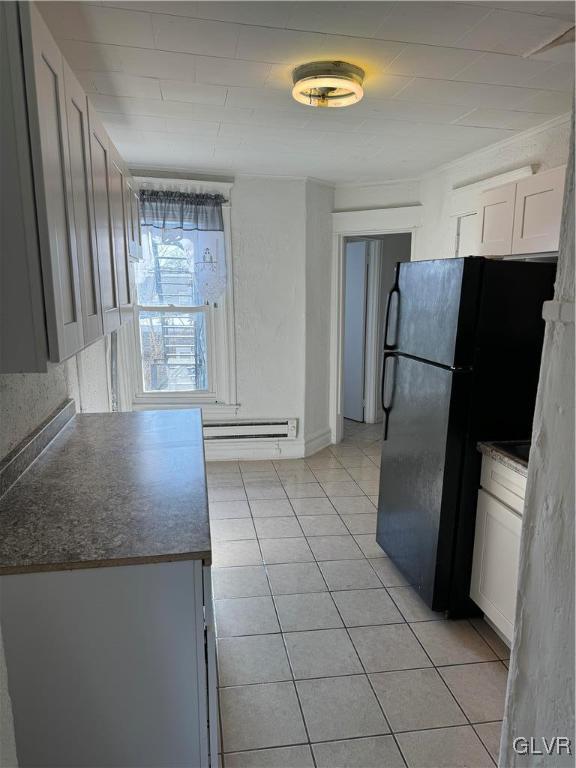 kitchen with white cabinets, light tile patterned flooring, baseboard heating, and black refrigerator