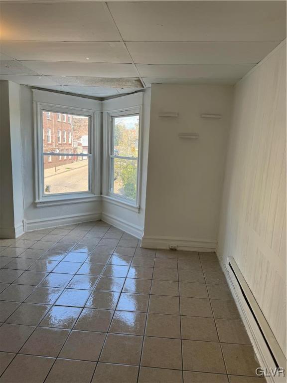 unfurnished room featuring a paneled ceiling, dark tile patterned floors, and a baseboard radiator