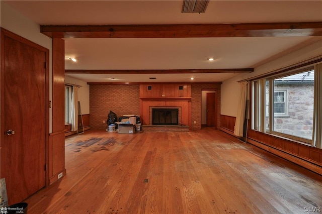 unfurnished living room with baseboard heating, hardwood / wood-style floors, a brick fireplace, and beam ceiling