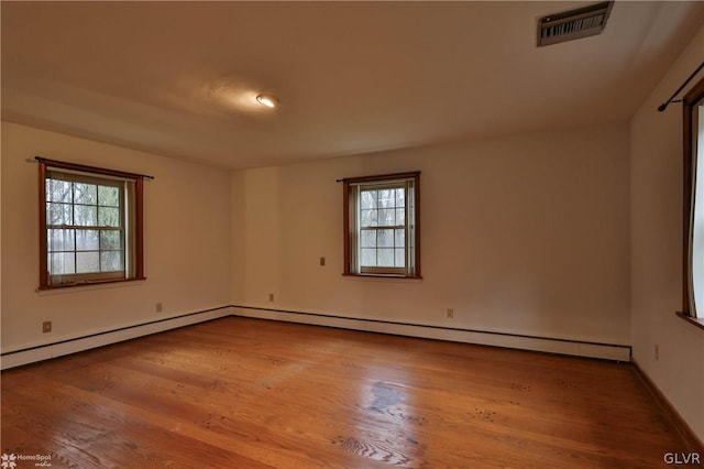 spare room featuring baseboard heating, hardwood / wood-style flooring, and plenty of natural light