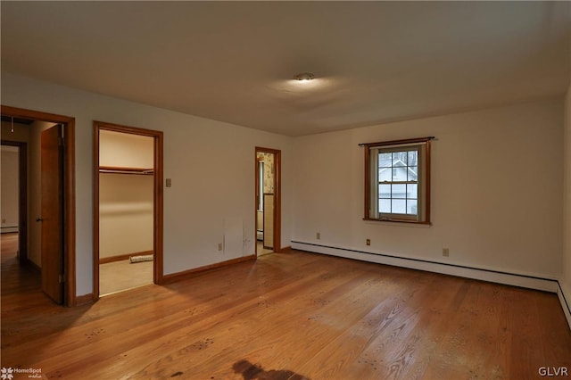 unfurnished bedroom with a walk in closet, baseboard heating, connected bathroom, and light hardwood / wood-style floors