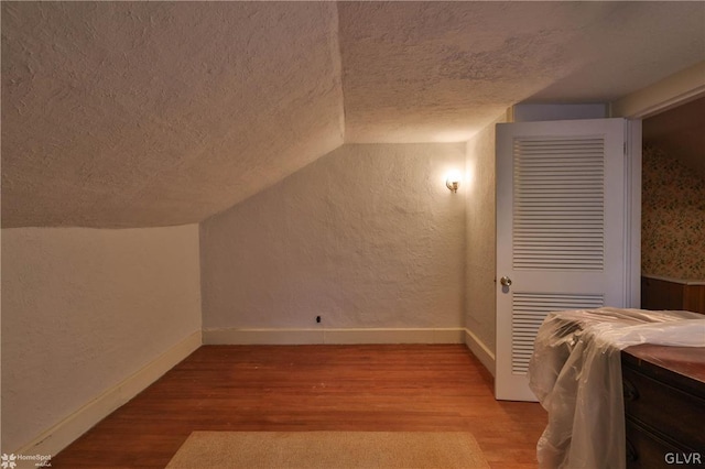 additional living space with lofted ceiling, a textured ceiling, and light hardwood / wood-style flooring