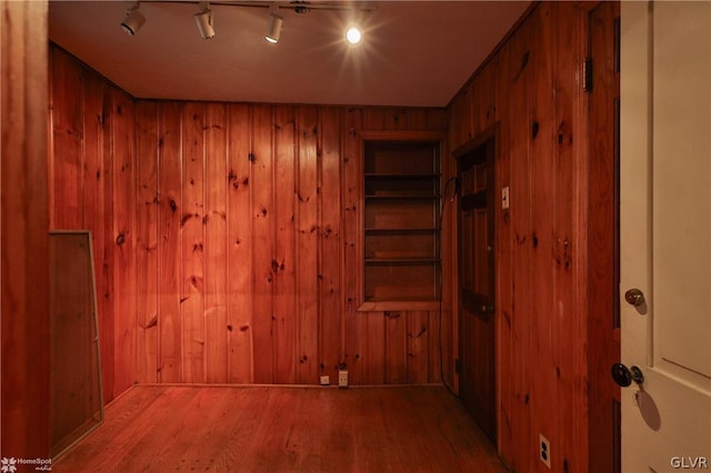 interior space with track lighting, wood-type flooring, and wood walls