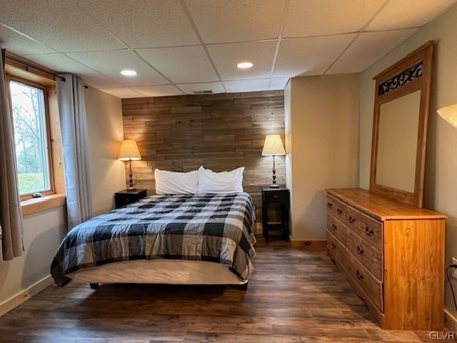 bedroom with wooden walls, dark hardwood / wood-style floors, and a drop ceiling