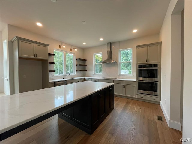 kitchen featuring stainless steel appliances, gray cabinets, sink, and wall chimney range hood