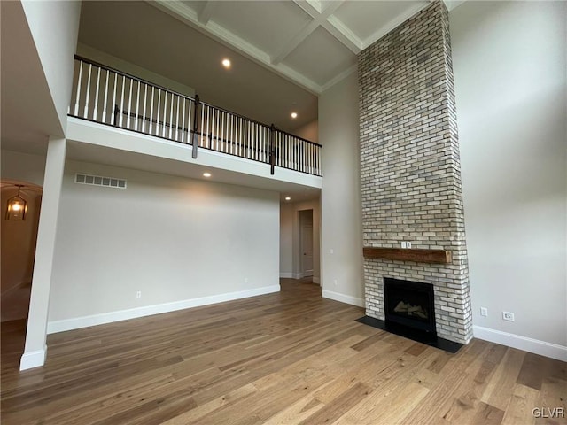 unfurnished living room featuring coffered ceiling, beam ceiling, light hardwood / wood-style flooring, a fireplace, and a high ceiling