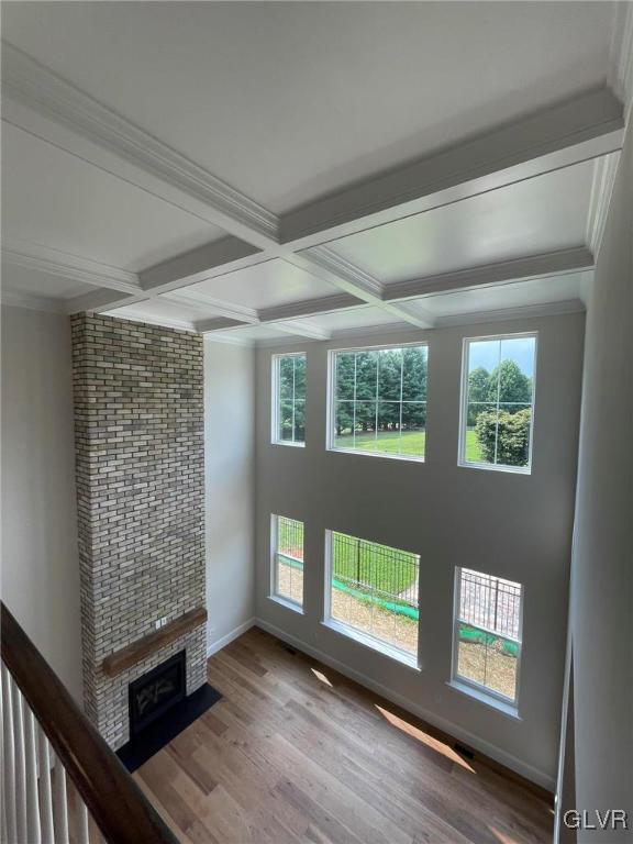 unfurnished living room featuring coffered ceiling, hardwood / wood-style flooring, crown molding, and beamed ceiling