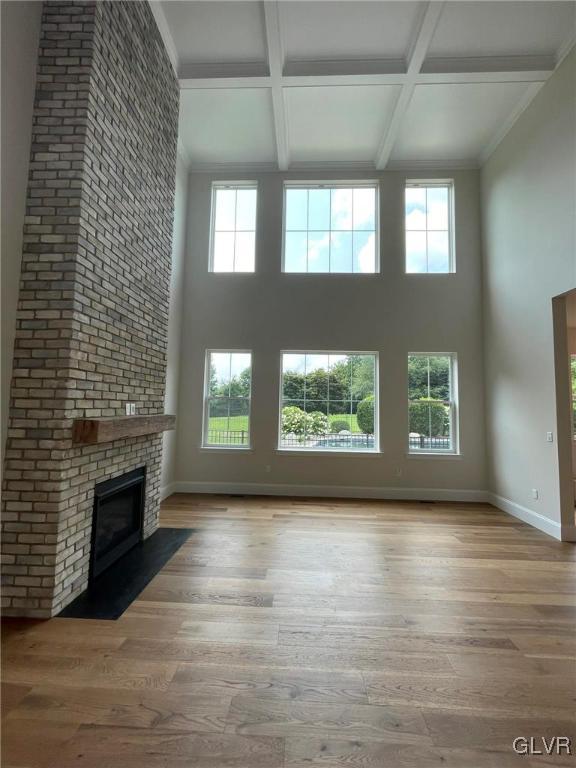 unfurnished living room with coffered ceiling, beam ceiling, a brick fireplace, and light wood-type flooring