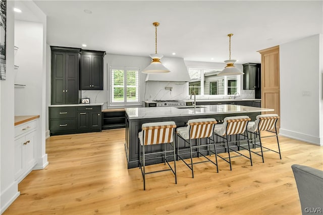 kitchen featuring sink, backsplash, a kitchen bar, light hardwood / wood-style floors, and a center island with sink