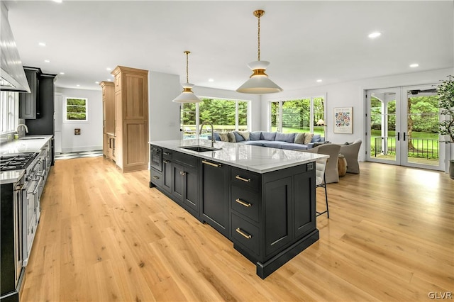 kitchen featuring decorative light fixtures, an island with sink, sink, light stone counters, and light wood-type flooring