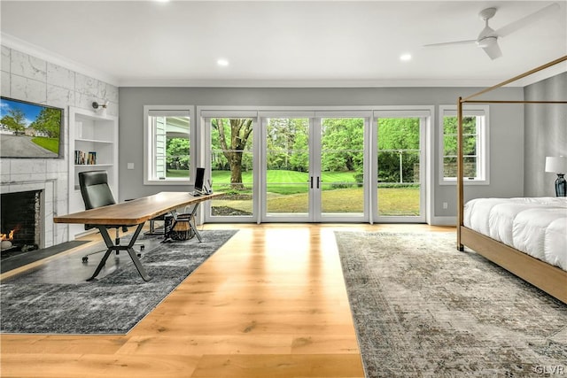 bedroom with crown molding, hardwood / wood-style flooring, ceiling fan, a fireplace, and access to outside