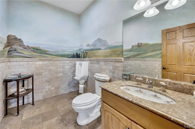 bathroom with toilet, a wainscoted wall, vanity, tile walls, and stone finish flooring