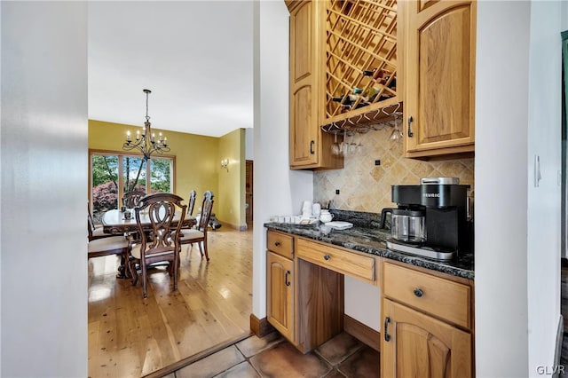 kitchen featuring a notable chandelier, tasteful backsplash, hanging light fixtures, dark stone counters, and tile patterned floors