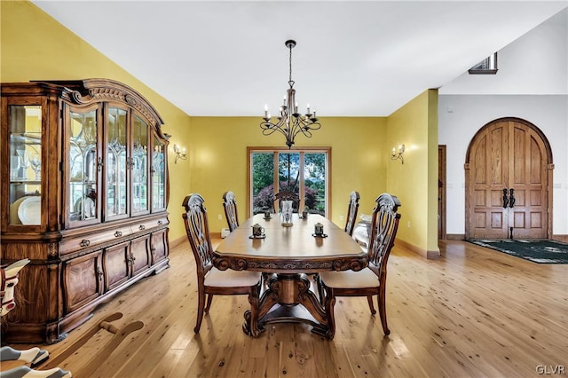 dining room with baseboards, light wood-style flooring, arched walkways, and a notable chandelier