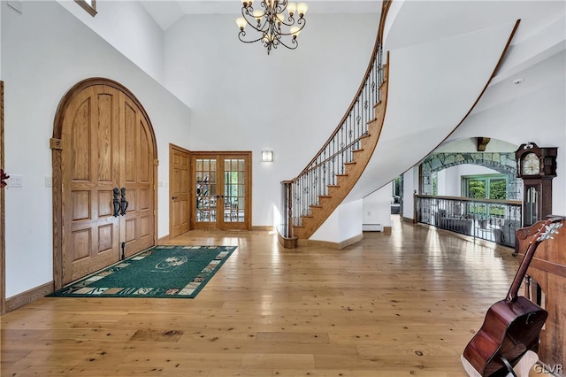 foyer entrance featuring arched walkways, french doors, wood-type flooring, and an inviting chandelier