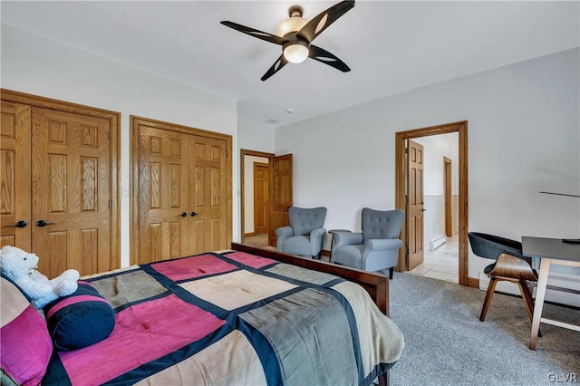 bedroom featuring a baseboard radiator, ceiling fan, ensuite bathroom, carpet, and multiple closets