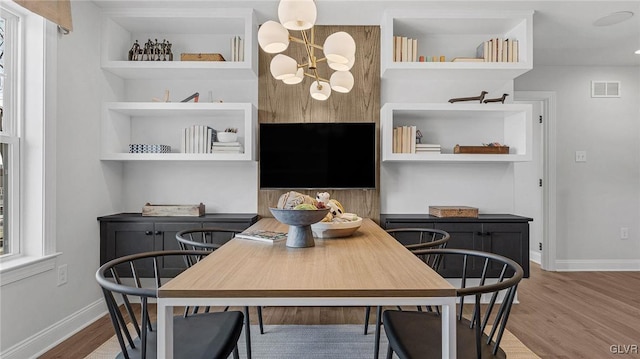 dining area with an inviting chandelier, built in shelves, and hardwood / wood-style flooring