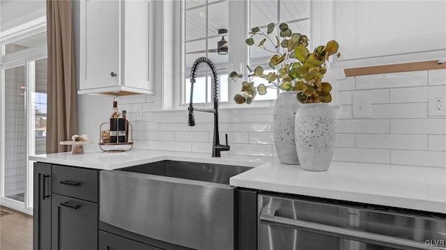 kitchen featuring stainless steel dishwasher, white cabinetry, sink, and backsplash