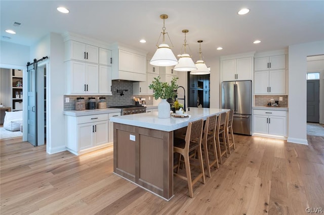 kitchen featuring high end fridge, light wood-type flooring, a center island with sink, and a barn door