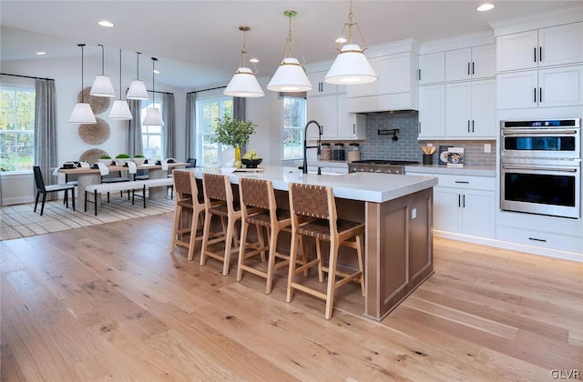 kitchen with decorative backsplash, light wood-type flooring, sink, a center island with sink, and appliances with stainless steel finishes