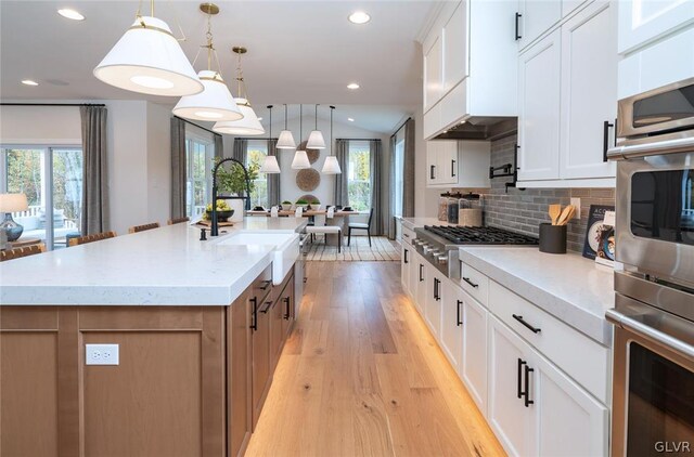 kitchen featuring a large island with sink, white cabinetry, decorative backsplash, and plenty of natural light