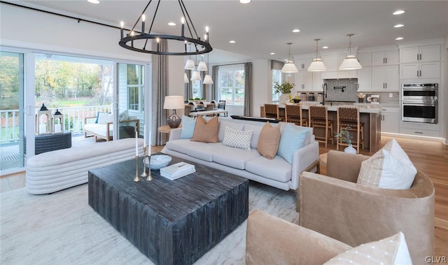 living room with sink, an inviting chandelier, plenty of natural light, and light wood-type flooring