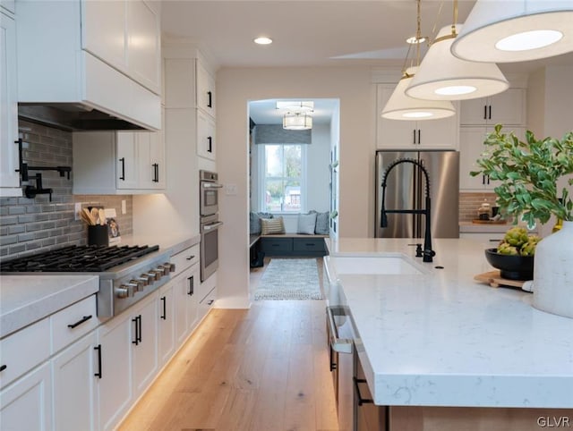 kitchen with white cabinetry, tasteful backsplash, light wood-type flooring, appliances with stainless steel finishes, and decorative light fixtures