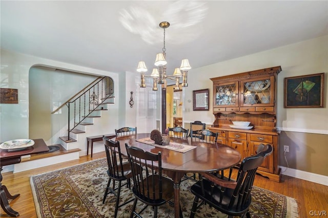 dining space with stairs, arched walkways, an inviting chandelier, and wood finished floors