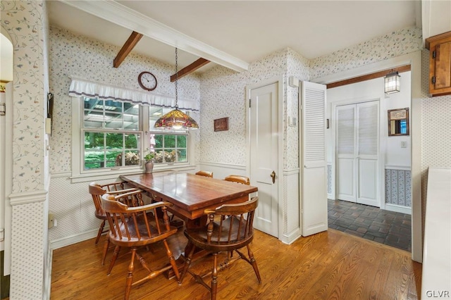 dining space featuring wallpapered walls, beam ceiling, a wainscoted wall, and wood finished floors