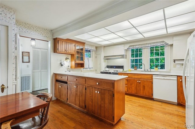 kitchen with white appliances, light wood finished floors, brown cabinetry, light countertops, and under cabinet range hood