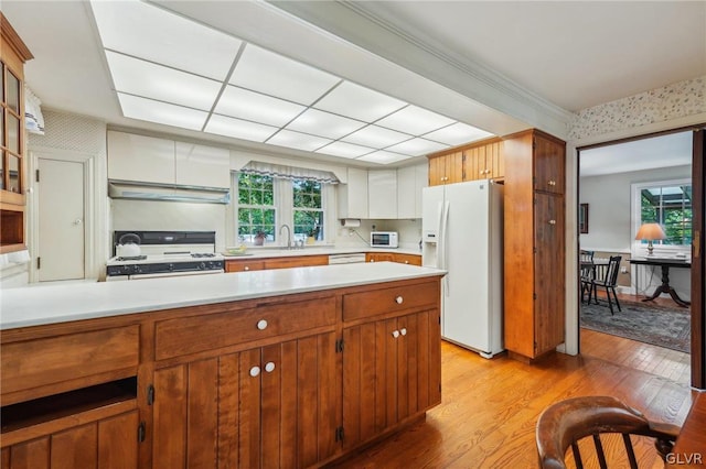 kitchen with brown cabinets, white appliances, under cabinet range hood, and light countertops