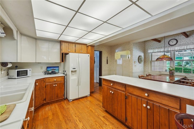 kitchen featuring brown cabinets, white appliances, light countertops, and wallpapered walls