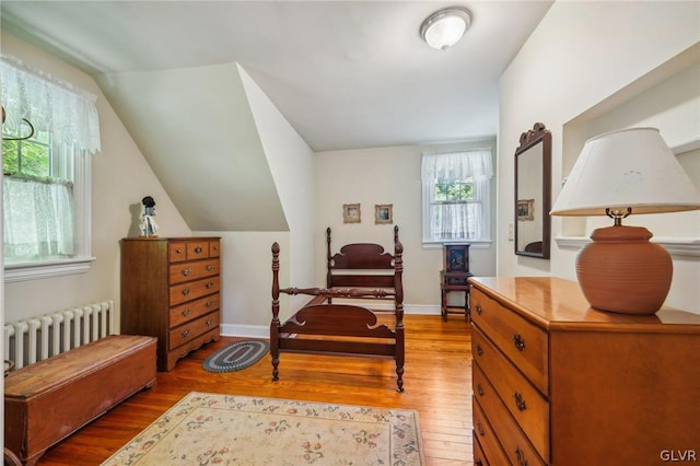 bedroom featuring lofted ceiling, radiator heating unit, light wood-style flooring, and baseboards