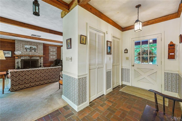 entrance foyer featuring wooden walls, wainscoting, beamed ceiling, brick floor, and a fireplace