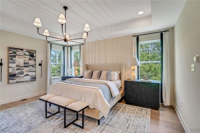 bedroom with a notable chandelier, hardwood / wood-style floors, and a raised ceiling