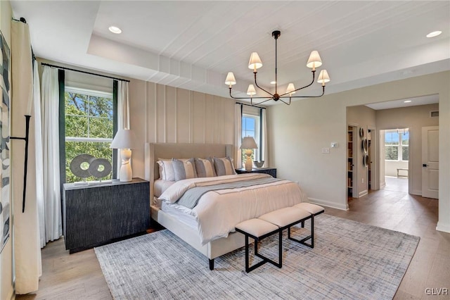 bedroom with a notable chandelier, light hardwood / wood-style floors, and a raised ceiling