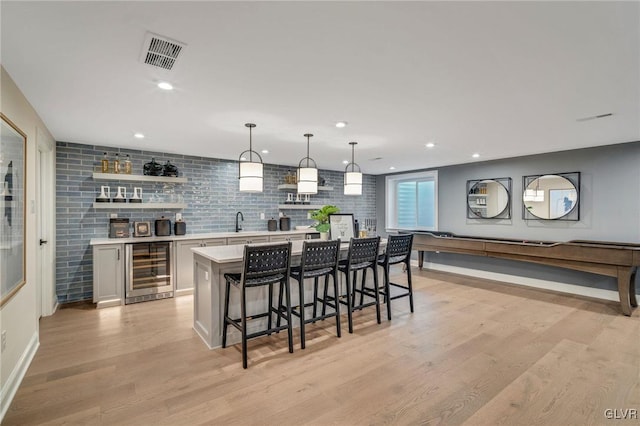 kitchen with a breakfast bar area, hanging light fixtures, light hardwood / wood-style floors, a kitchen island, and beverage cooler