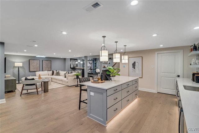 kitchen with hanging light fixtures, gray cabinets, light wood-type flooring, and a kitchen bar