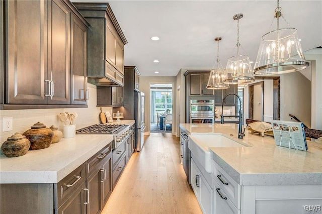 kitchen with appliances with stainless steel finishes, light hardwood / wood-style flooring, tasteful backsplash, light stone counters, and hanging light fixtures