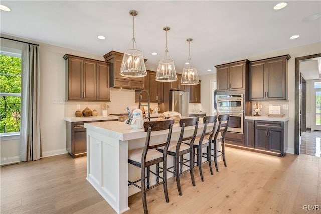 kitchen with stainless steel appliances, hanging light fixtures, a kitchen bar, a center island with sink, and light hardwood / wood-style floors