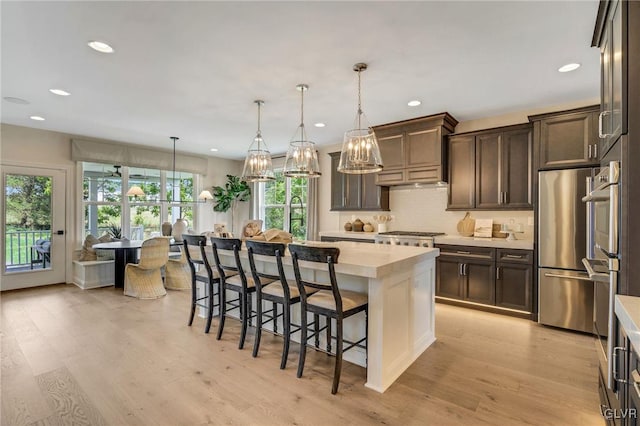 kitchen featuring pendant lighting, a kitchen island, dark brown cabinetry, light hardwood / wood-style floors, and stainless steel refrigerator