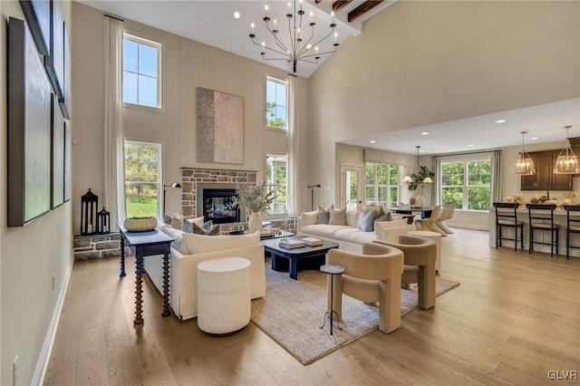 living room featuring light hardwood / wood-style floors, a notable chandelier, a fireplace, and a towering ceiling