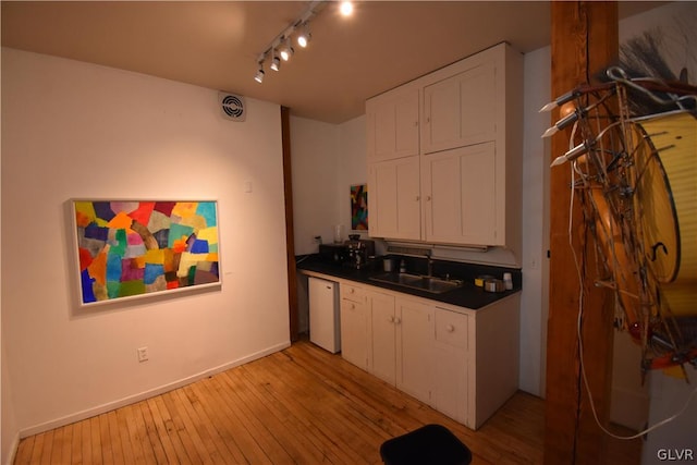 kitchen featuring dishwasher, sink, white cabinets, rail lighting, and light hardwood / wood-style flooring